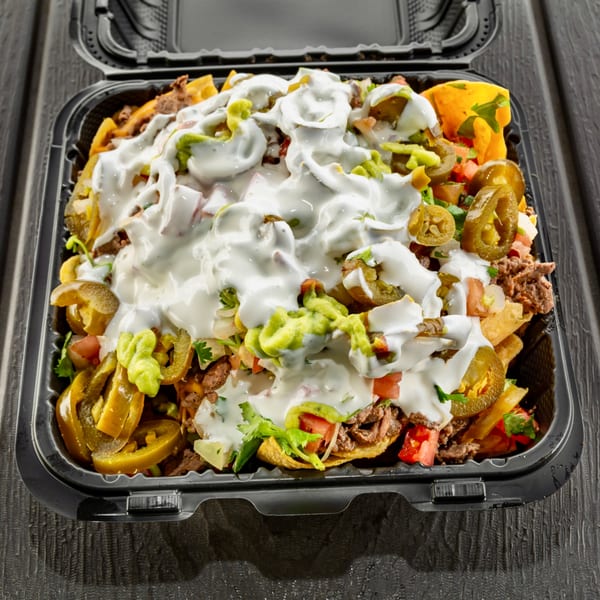 Sabor Tacos' nachos with meat, jalapeños, guacamole, and sour cream in a black takeout container.