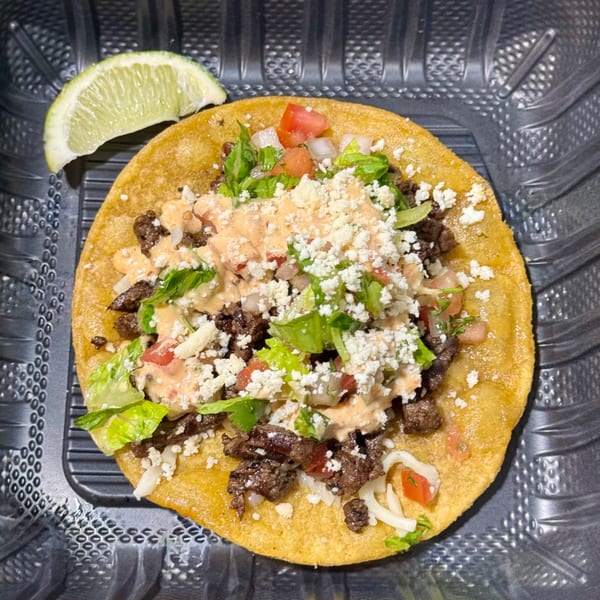 Sabor Tacos' carne asada tostada with lettuce, tomatoes, cheese, and sauce, served with a lime wedge.