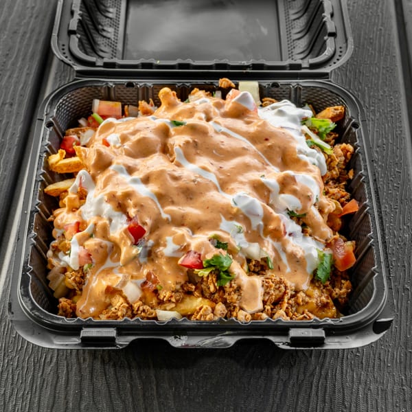 Sabor Tacos' loaded fries with meat, cheese sauce, sour cream, tomatoes, and cilantro in a to-go container.