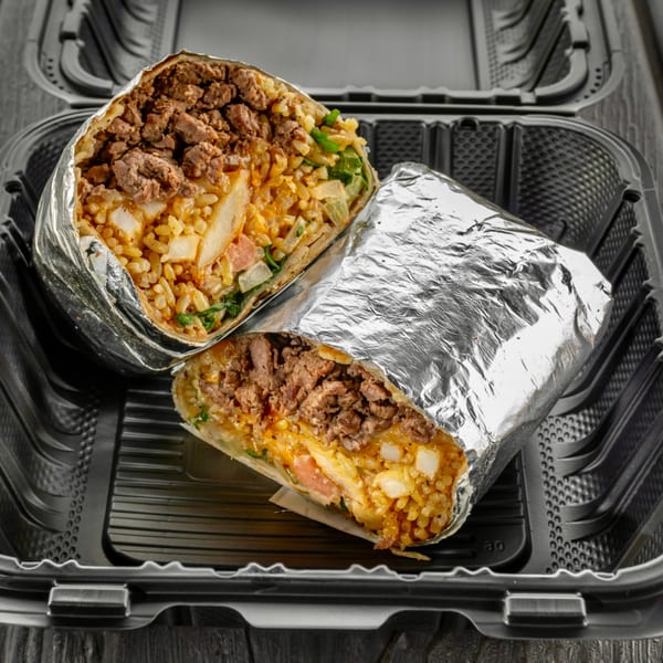 A Sabor Tacos burrito, cut in half, revealing meat, rice, and vegetables, in a to-go container.