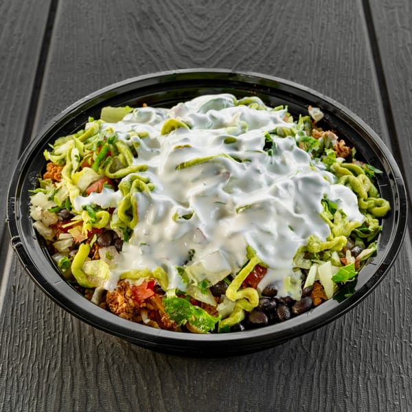 Sabor Tacos' Mexican burrito bowl with meat, beans, lettuce, and sour cream on a dark table.