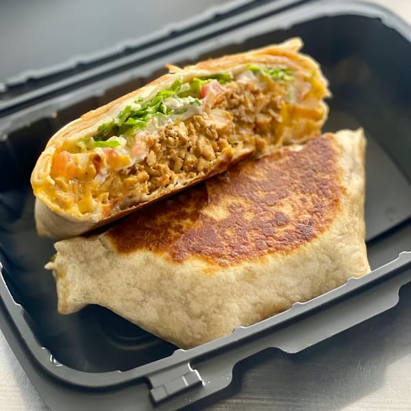 A Sabor Tacos burrito, cut in half, revealing chicken, lettuce, and sauce inside a toasted tortilla.